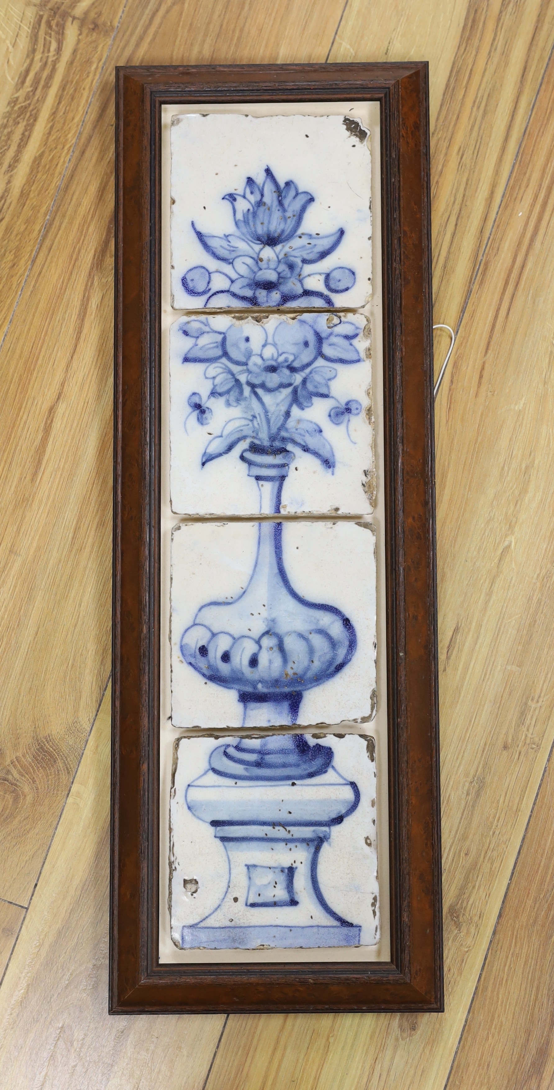 A 17th century Delft four tile framed panel, painted in underglaze blue with a vase of flowers on a pedestal, 64 cms high